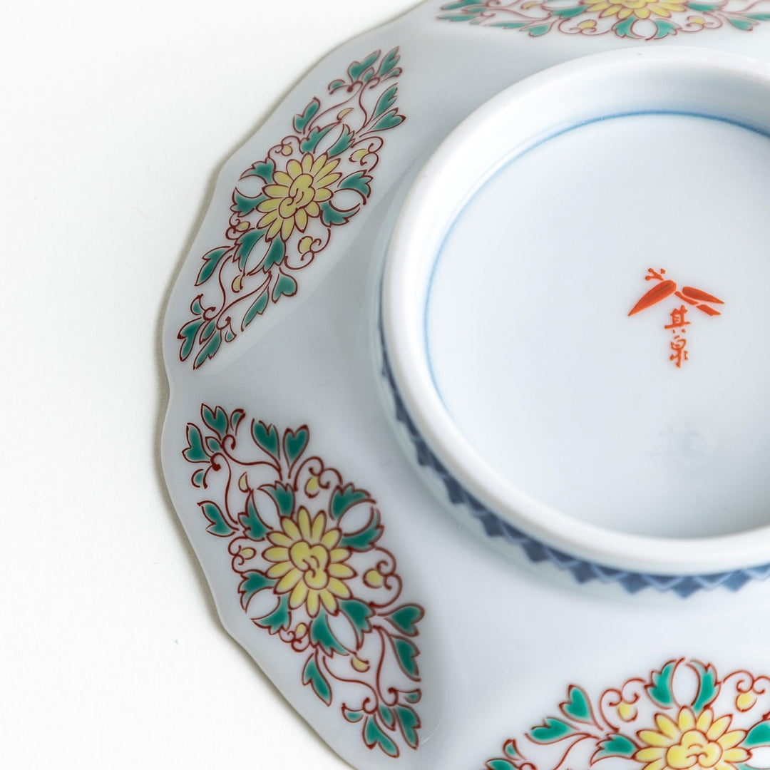 A sauce dish with a blue geometric pattern in the center and ornate floral designs in red, green, and gold on the scalloped rim.