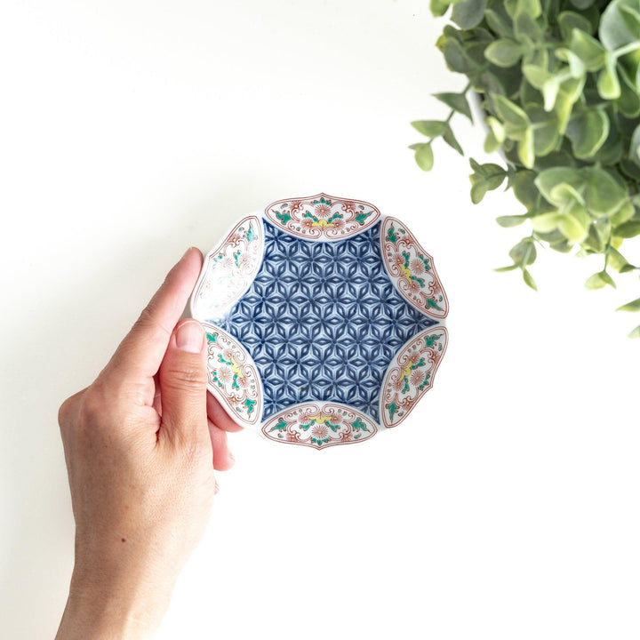 A sauce dish with a blue geometric pattern in the center and ornate floral designs in red, green, and gold on the scalloped rim.