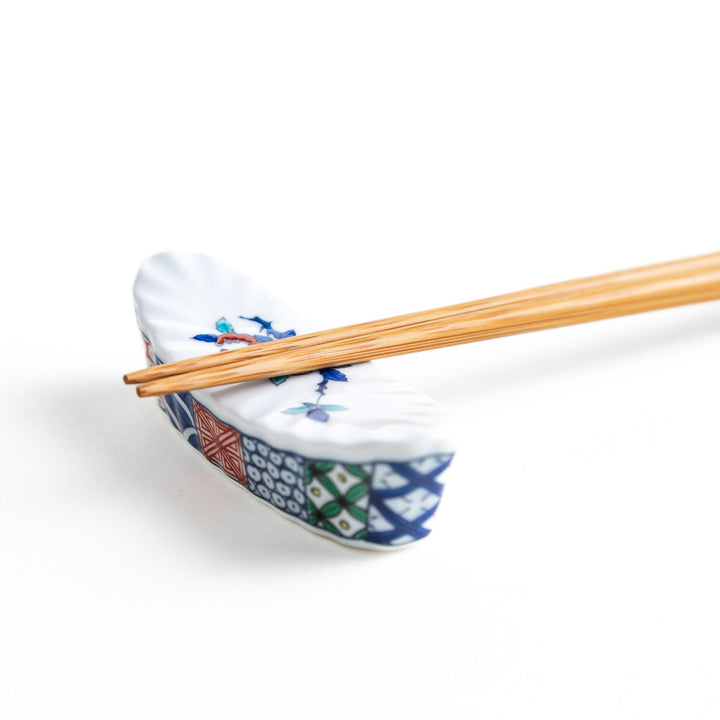 A ceramic chopstick rest with a floral design on top and a colorful geometric pattern along the sides.