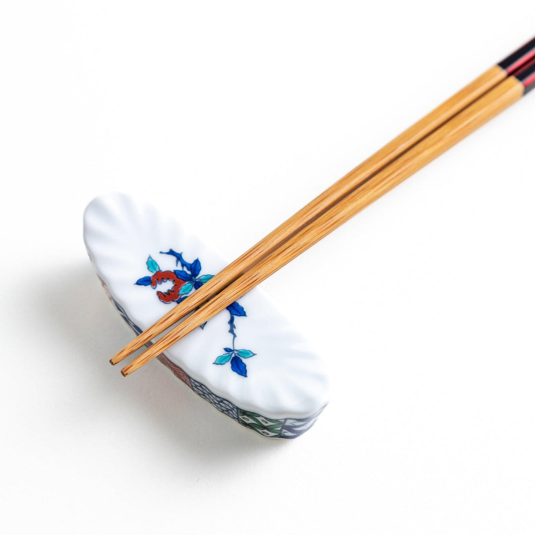 A ceramic chopstick rest with a floral design on top and a colorful geometric pattern along the sides.