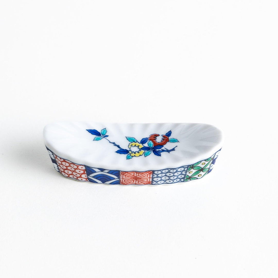 A ceramic chopstick rest with a floral design on top and a colorful geometric pattern along the sides.