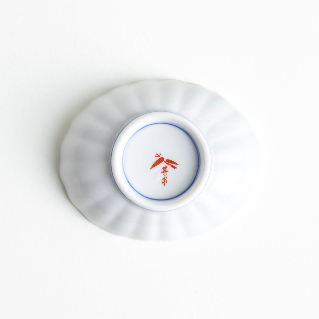 A small condiment bowl with a white interior and a scalloped edge, decorated with a central floral motif and colorful geometric patterns in blue, red, and green.