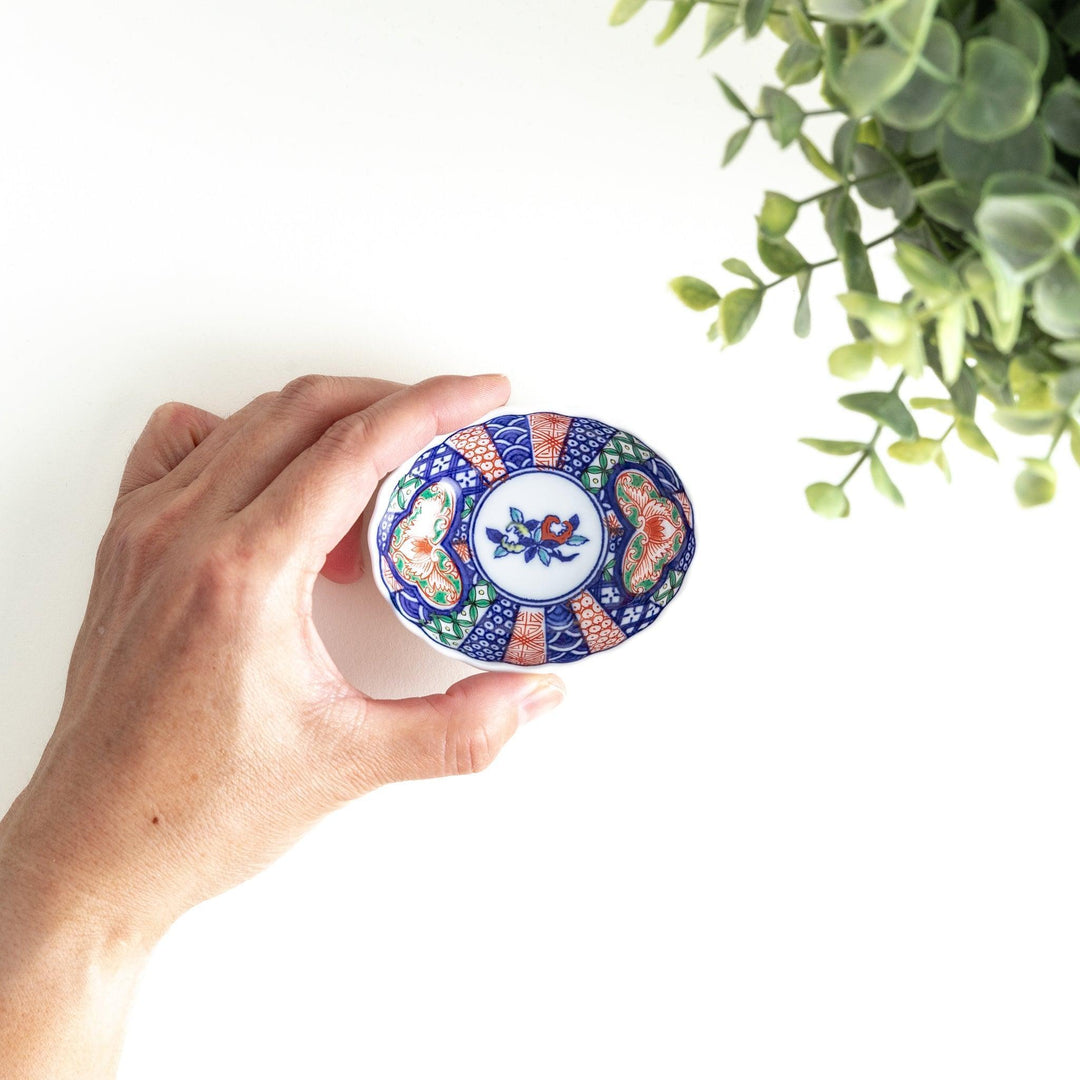 A small condiment bowl with a white interior and a scalloped edge, decorated with a central floral motif and colorful geometric patterns in blue, red, and green.