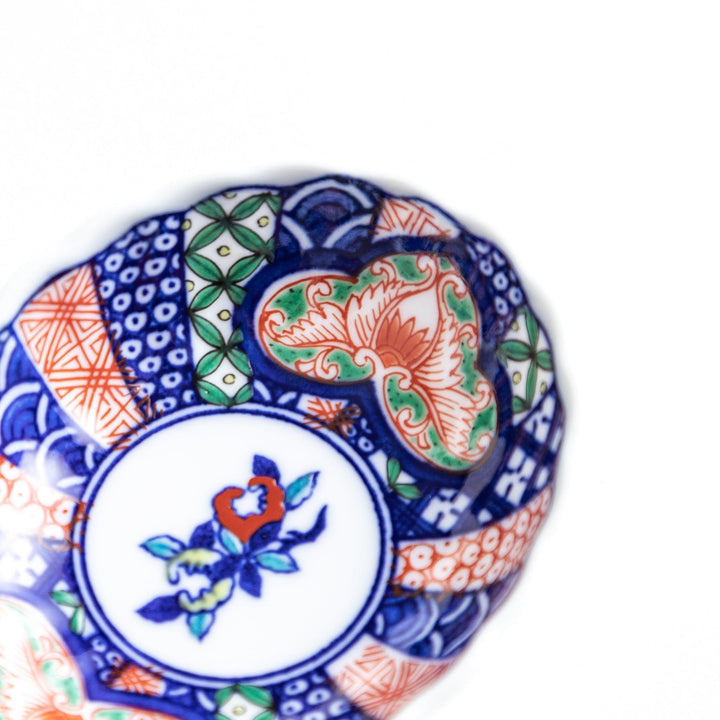 A small condiment bowl with a white interior and a scalloped edge, decorated with a central floral motif and colorful geometric patterns in blue, red, and green.