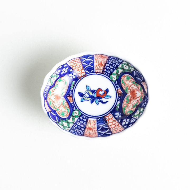 A small condiment bowl with a white interior and a scalloped edge, decorated with a central floral motif and colorful geometric patterns in blue, red, and green.