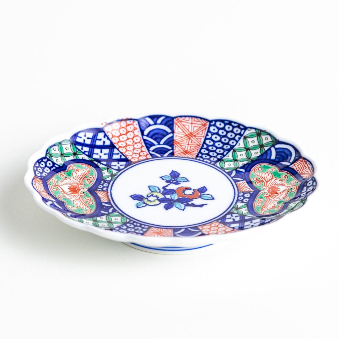 A sauce dish with a central floral motif and an intricate multicolored geometric pattern on the scalloped rim.