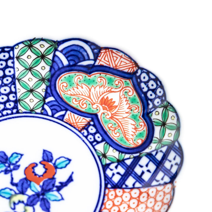 A sauce dish with a central floral motif and an intricate multicolored geometric pattern on the scalloped rim.