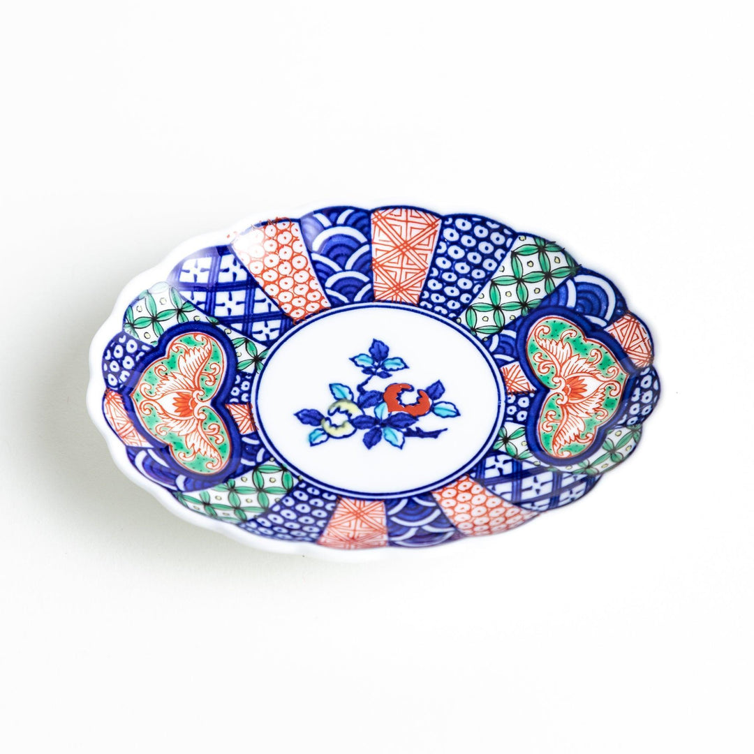 A sauce dish with a central floral motif and an intricate multicolored geometric pattern on the scalloped rim.