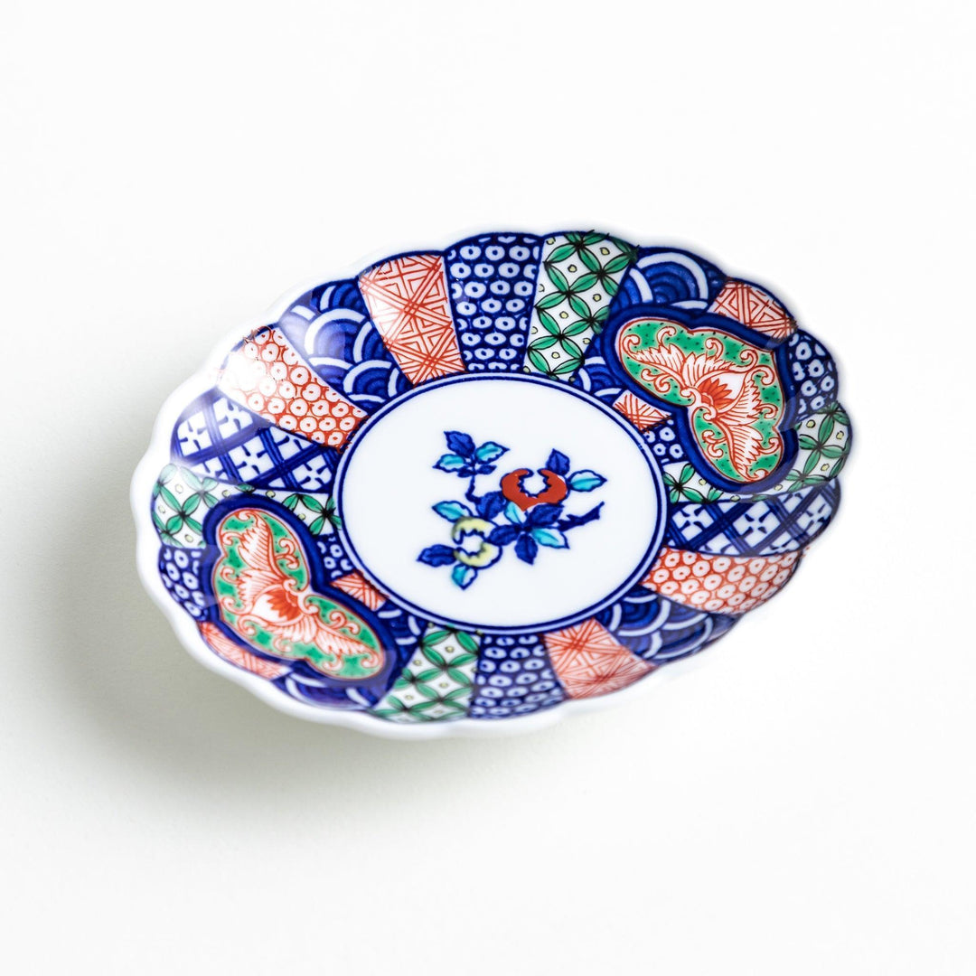 A sauce dish with a central floral motif and an intricate multicolored geometric pattern on the scalloped rim.