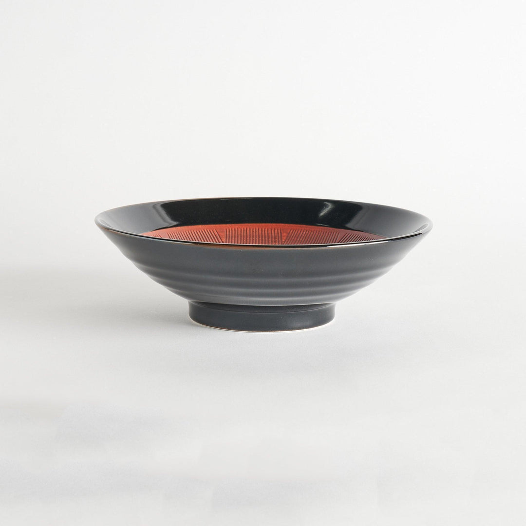 A shallow bowl with a smooth black exterior and a textured red interior.