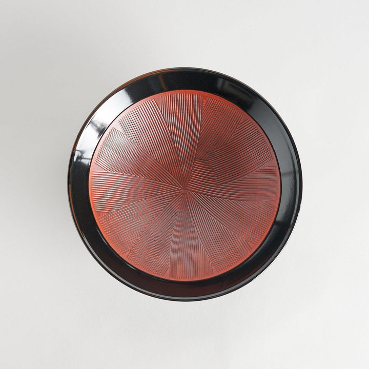 A shallow bowl with a smooth black exterior and a textured red interior.