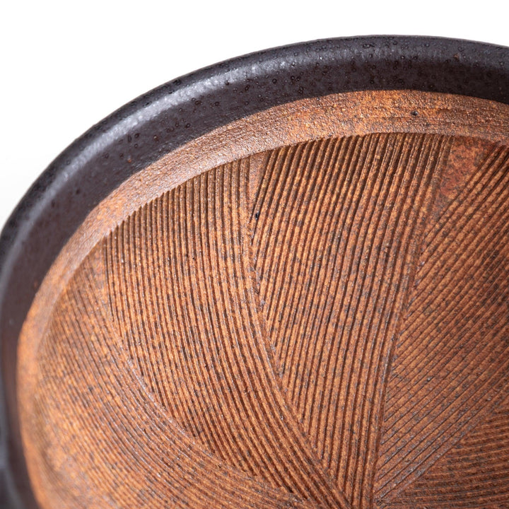 A small, black ceramic bowl with a rough texture and a natural, unglazed bottom.
