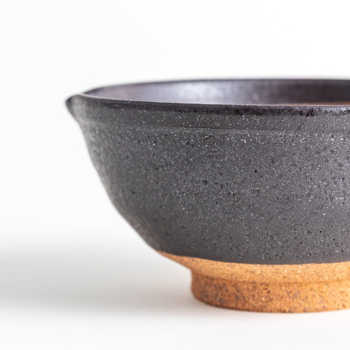 A small, black ceramic bowl with a rough texture and a natural, unglazed bottom.
