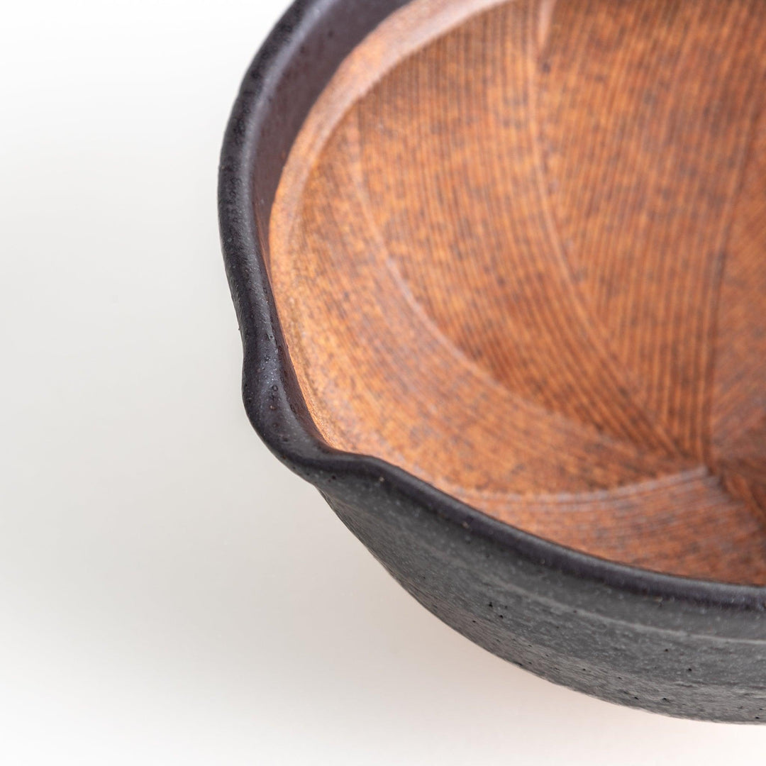 A small, black ceramic bowl with a rough texture and a natural, unglazed bottom.
