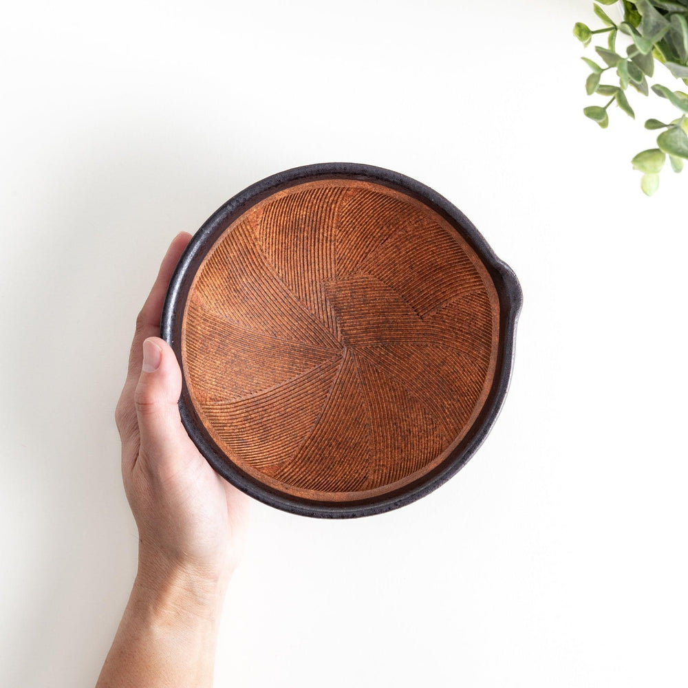 A small, black ceramic bowl with a rough texture and a natural, unglazed bottom.
