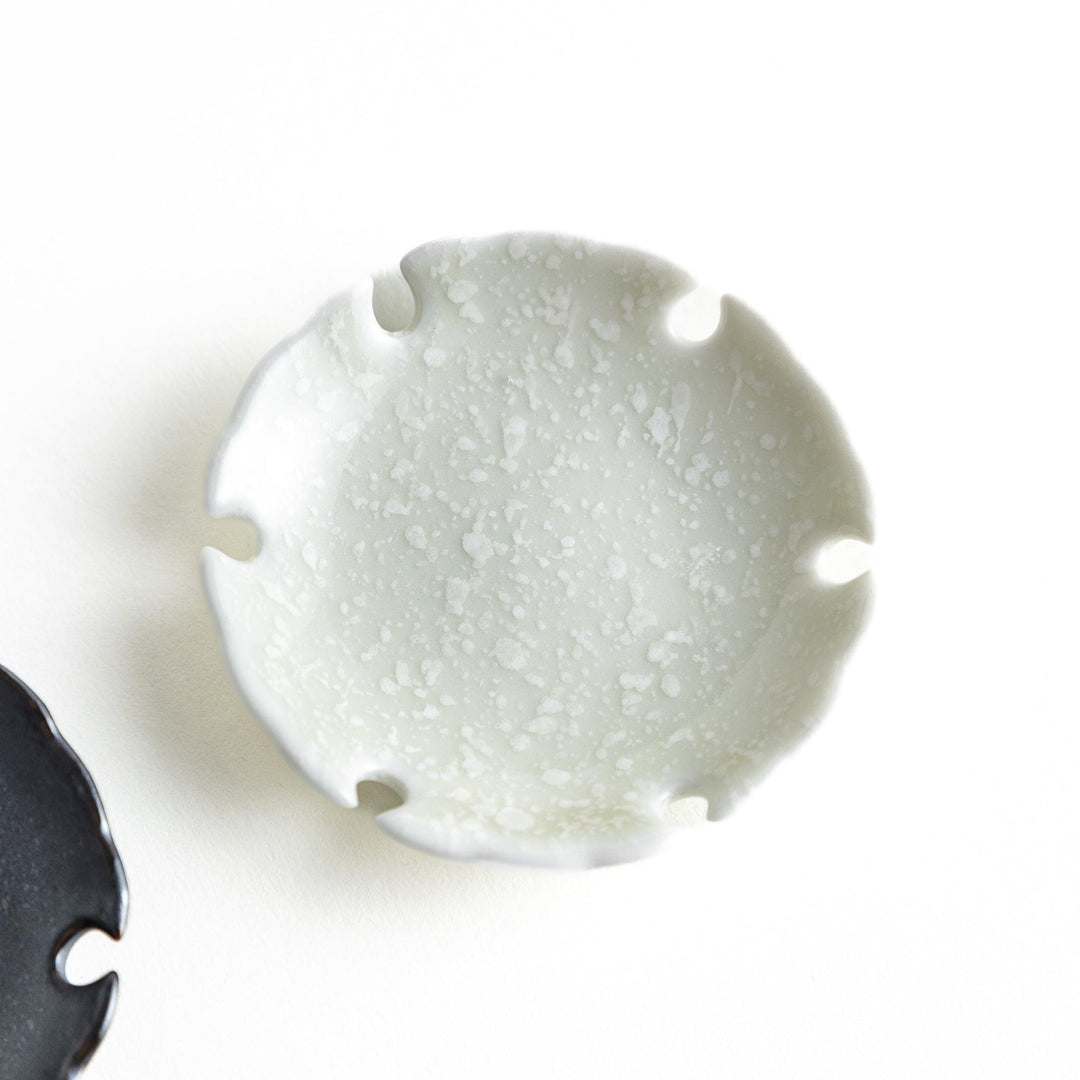 A pair of small black and white round ceramic chopstick rests with a scalloped edge.