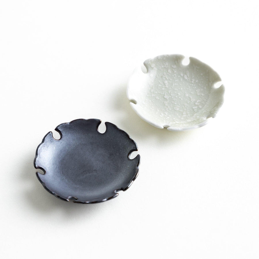 A pair of small black and white round ceramic chopstick rests with a scalloped edge.