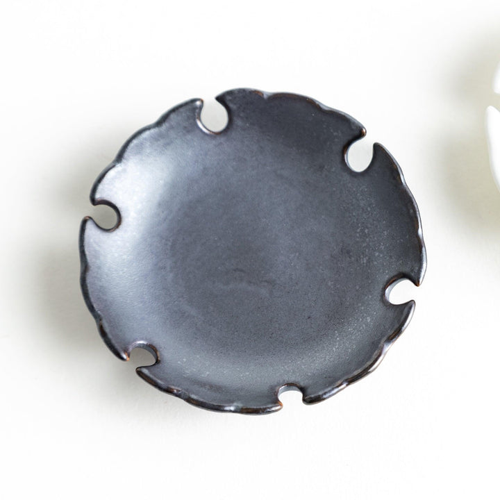 A pair of small black and white round ceramic chopstick rests with a scalloped edge.