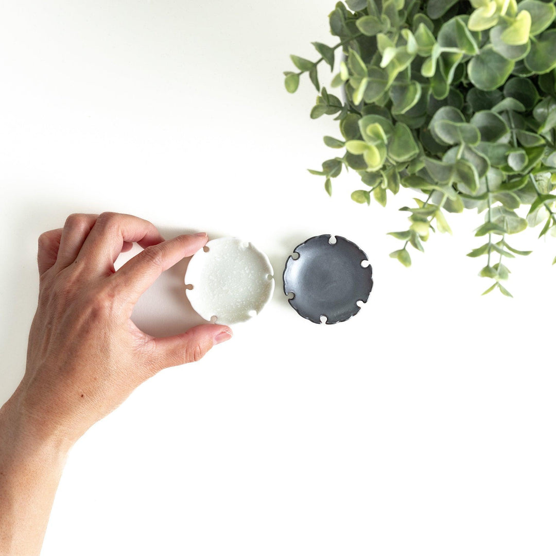 A pair of small black and white round ceramic chopstick rests with a scalloped edge.