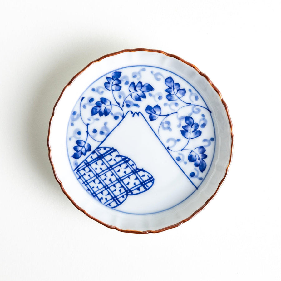 A ceramic dish with a blue and white design, showcasing a pattern of floral motifs and a depiction of Mount Fuji.