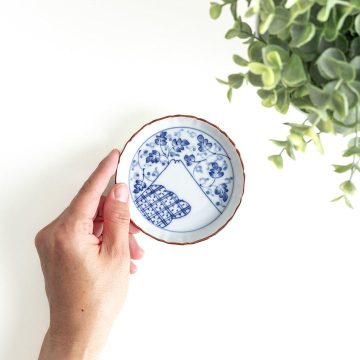 A ceramic dish with a blue and white design, showcasing a pattern of floral motifs and a depiction of Mount Fuji.