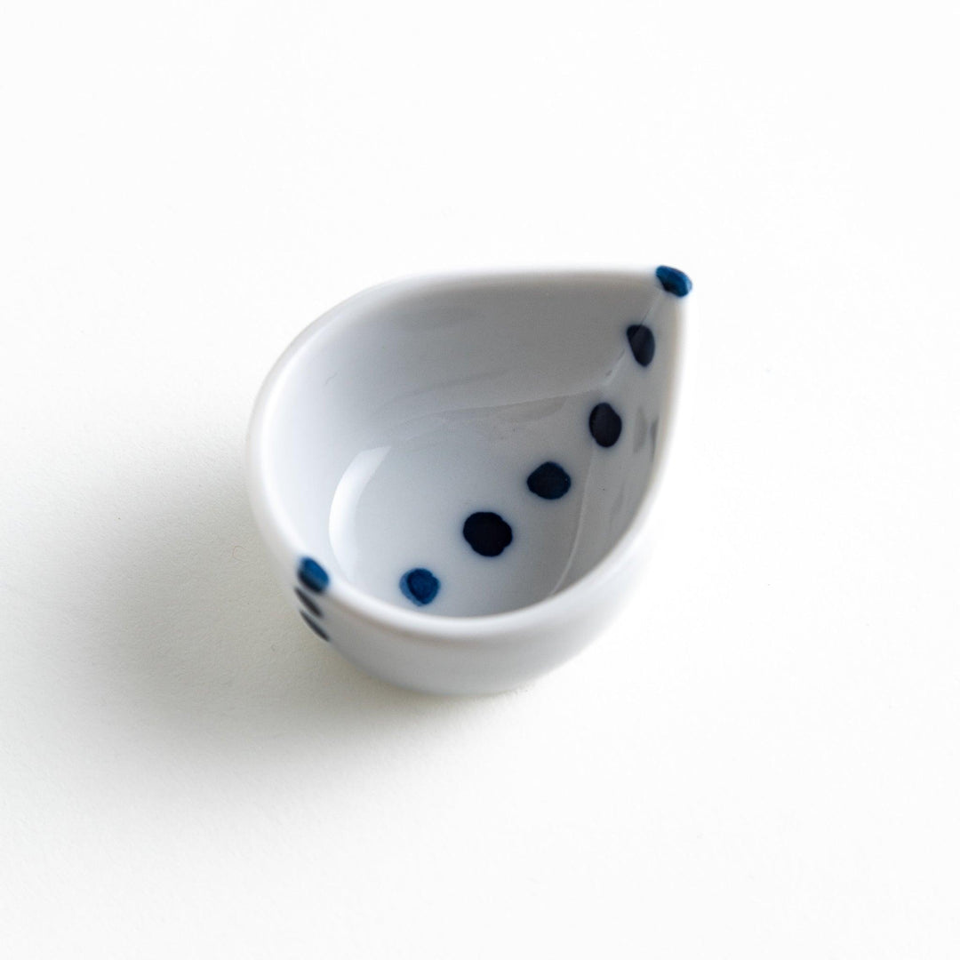 A small, curved condiment bowl with minimal blue dot accents.