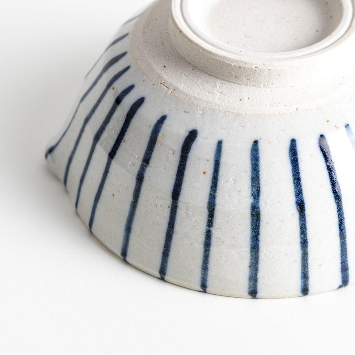 A small, white ceramic bowl with blue vertical stripes on the exterior and a dark brown, textured interior.