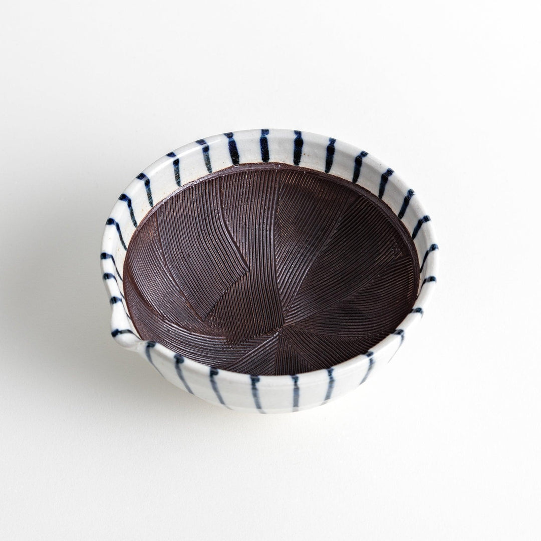 A small, white ceramic bowl with blue vertical stripes on the exterior and a dark brown, textured interior.