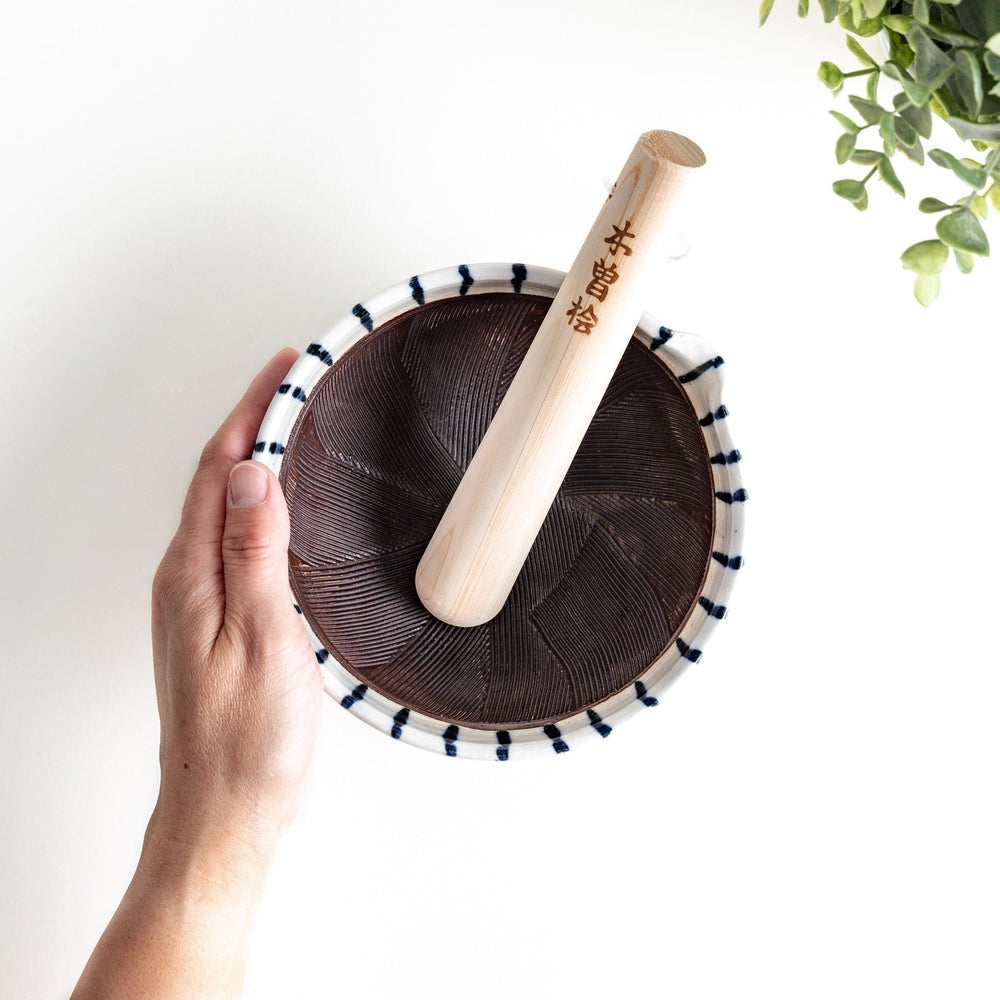 A small, white ceramic bowl with blue vertical stripes on the exterior and a dark brown, textured interior.