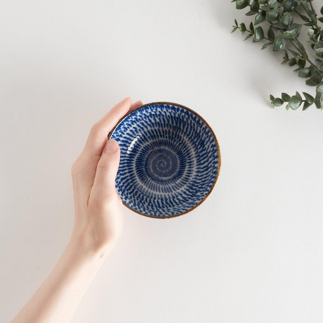 A round dessert bowl adorned with a sprial blue pattern spreading from the center.