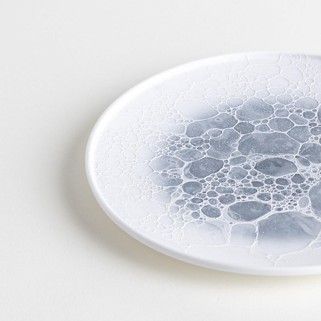 A white dessert plate featuring a unique bubble design in shades of blue, resembling frothy ocean waves.