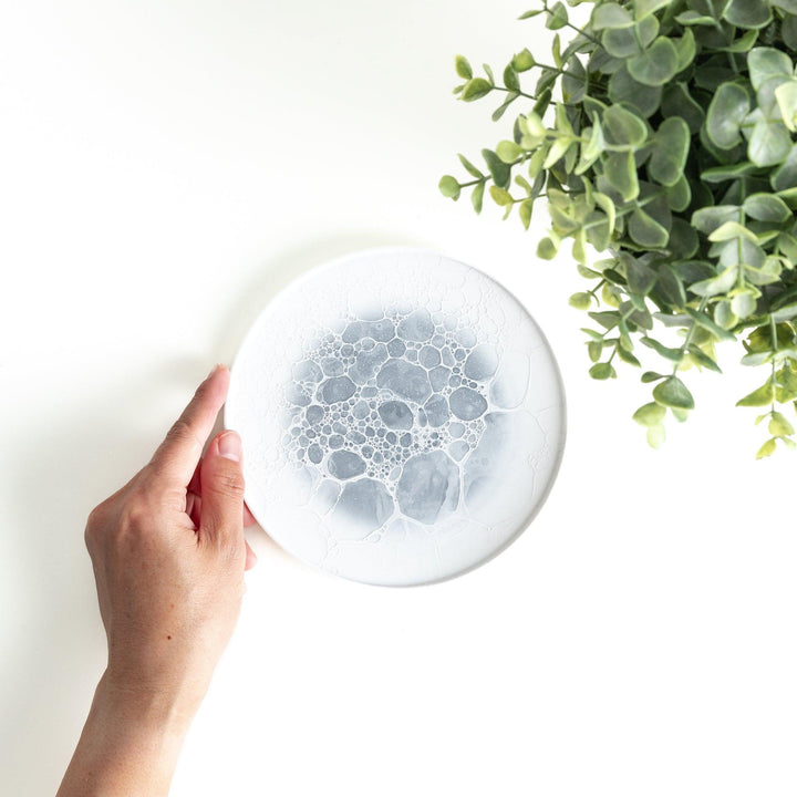 A white dessert plate featuring a unique bubble design in shades of blue, resembling frothy ocean waves.