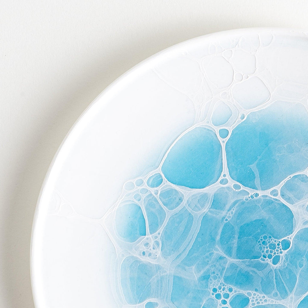 A white dessert plate featuring a unique bubble design in shades of blue, resembling frothy ocean waves.