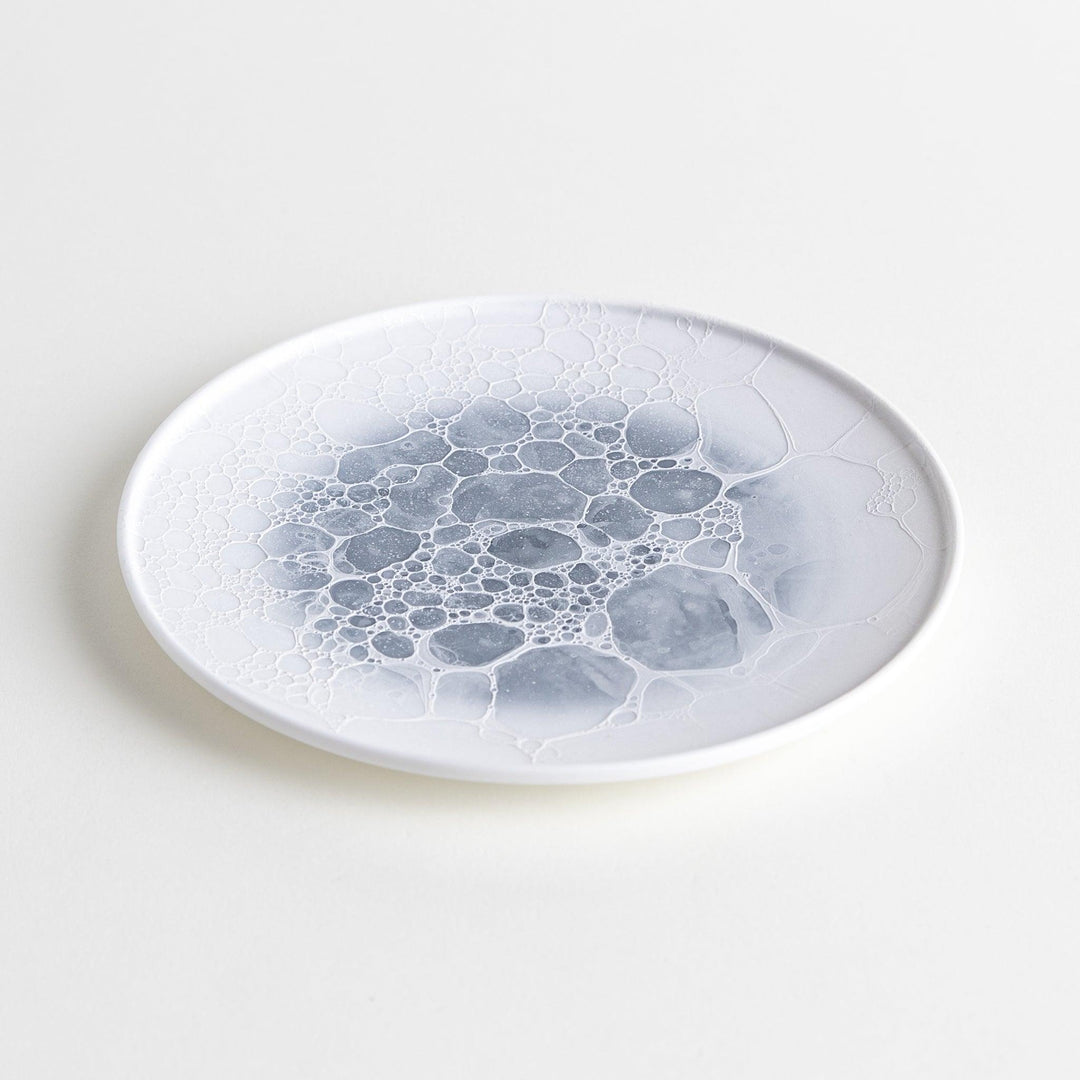 A white dessert plate featuring a unique bubble design in shades of blue, resembling frothy ocean waves.