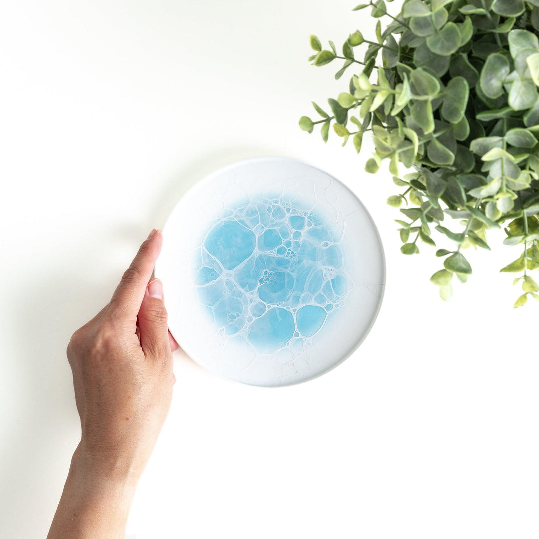 A white dessert plate featuring a unique bubble design in shades of blue, resembling frothy ocean waves.