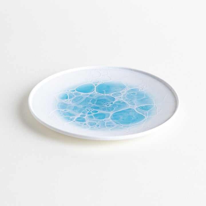 A white dessert plate featuring a unique bubble design in shades of blue, resembling frothy ocean waves.