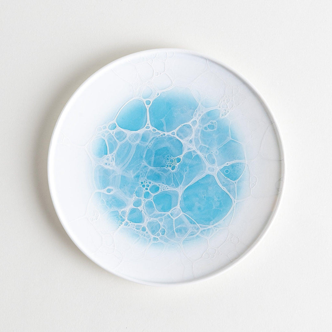 A white dessert plate featuring a unique bubble design in shades of blue, resembling frothy ocean waves.