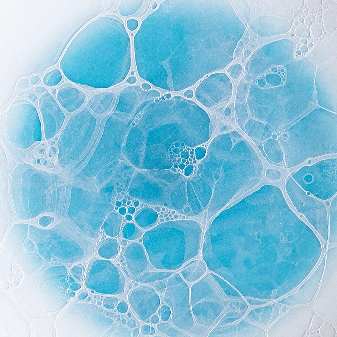 A white dessert plate featuring a unique bubble design in shades of blue, resembling frothy ocean waves.