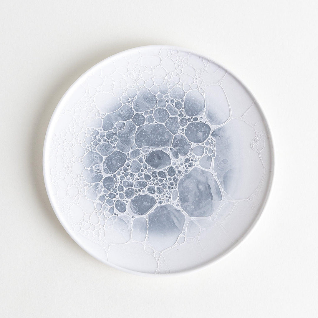 A white dessert plate featuring a unique bubble design in shades of blue, resembling frothy ocean waves.