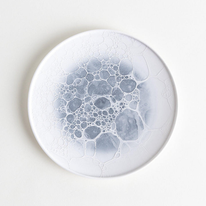 A white dessert plate featuring a unique bubble design in shades of blue, resembling frothy ocean waves.