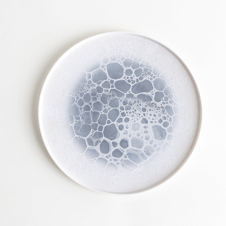 A white dinner plate featuring a unique bubble design in shades of blue, resembling frothy ocean waves.