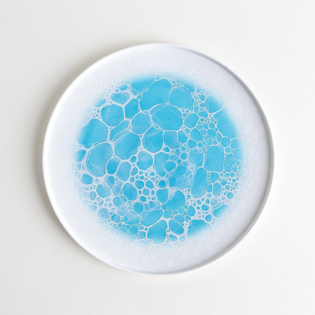 A white dinner plate featuring a unique bubble design in shades of blue, resembling frothy ocean waves.