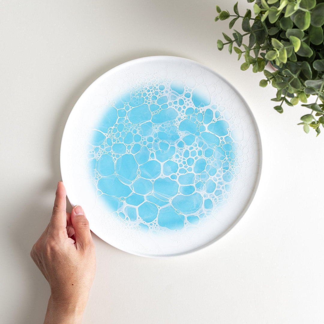 A white dinner plate featuring a unique bubble design in shades of blue, resembling frothy ocean waves.