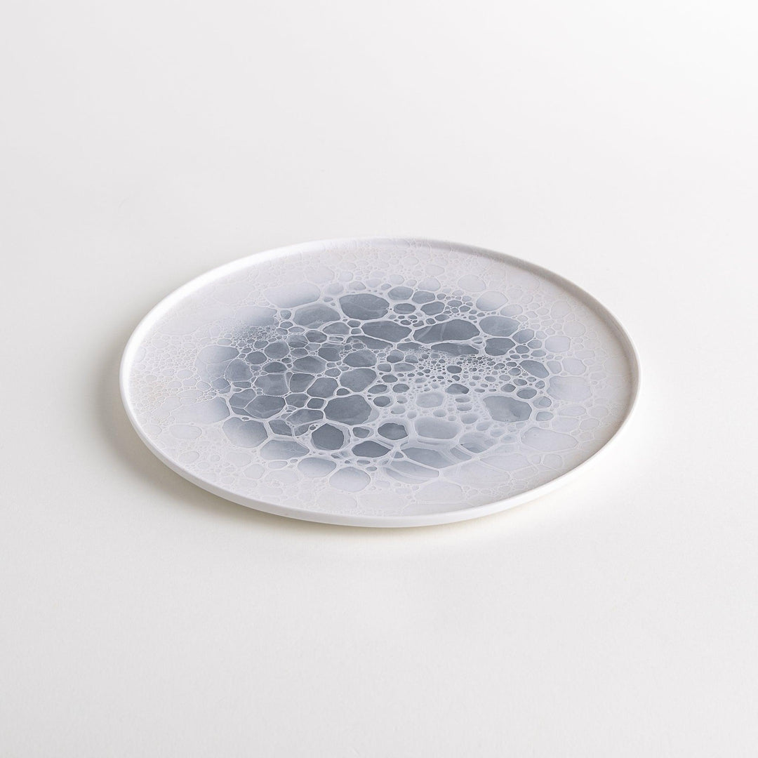 A white dinner plate featuring a unique bubble design in shades of blue, resembling frothy ocean waves.