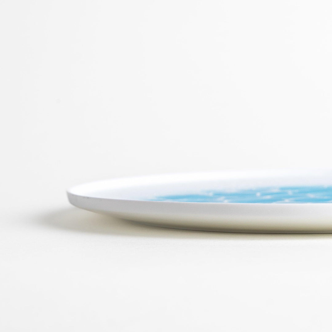 A white dinner plate featuring a unique bubble design in shades of blue, resembling frothy ocean waves.