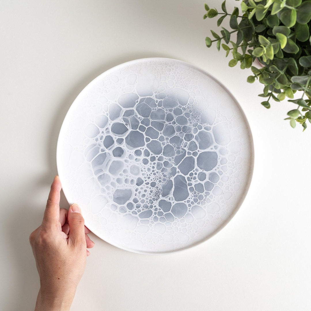 A white dinner plate featuring a unique bubble design in shades of blue, resembling frothy ocean waves.