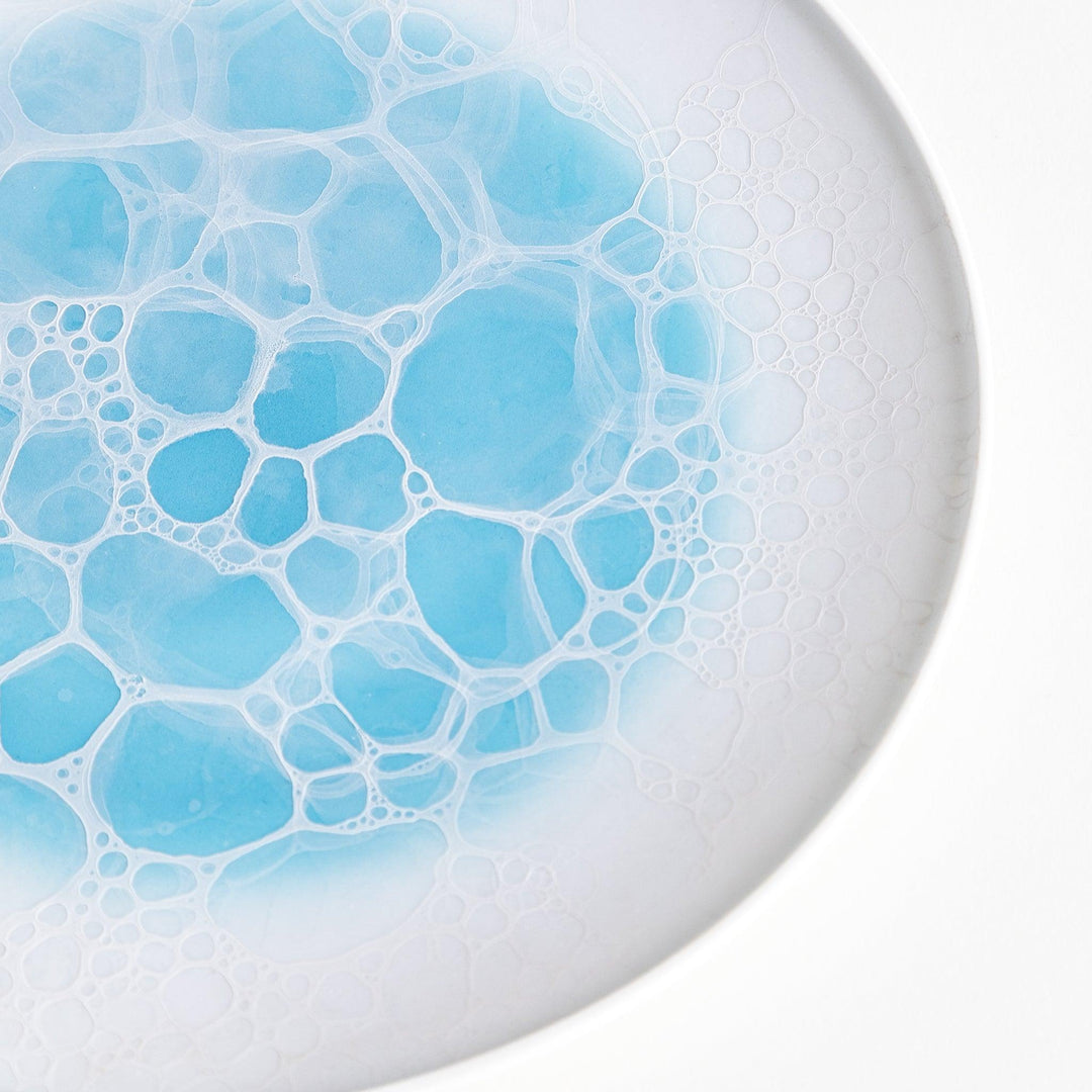 A white salad plate featuring a unique bubble design in shades of blue, resembling frothy ocean waves.