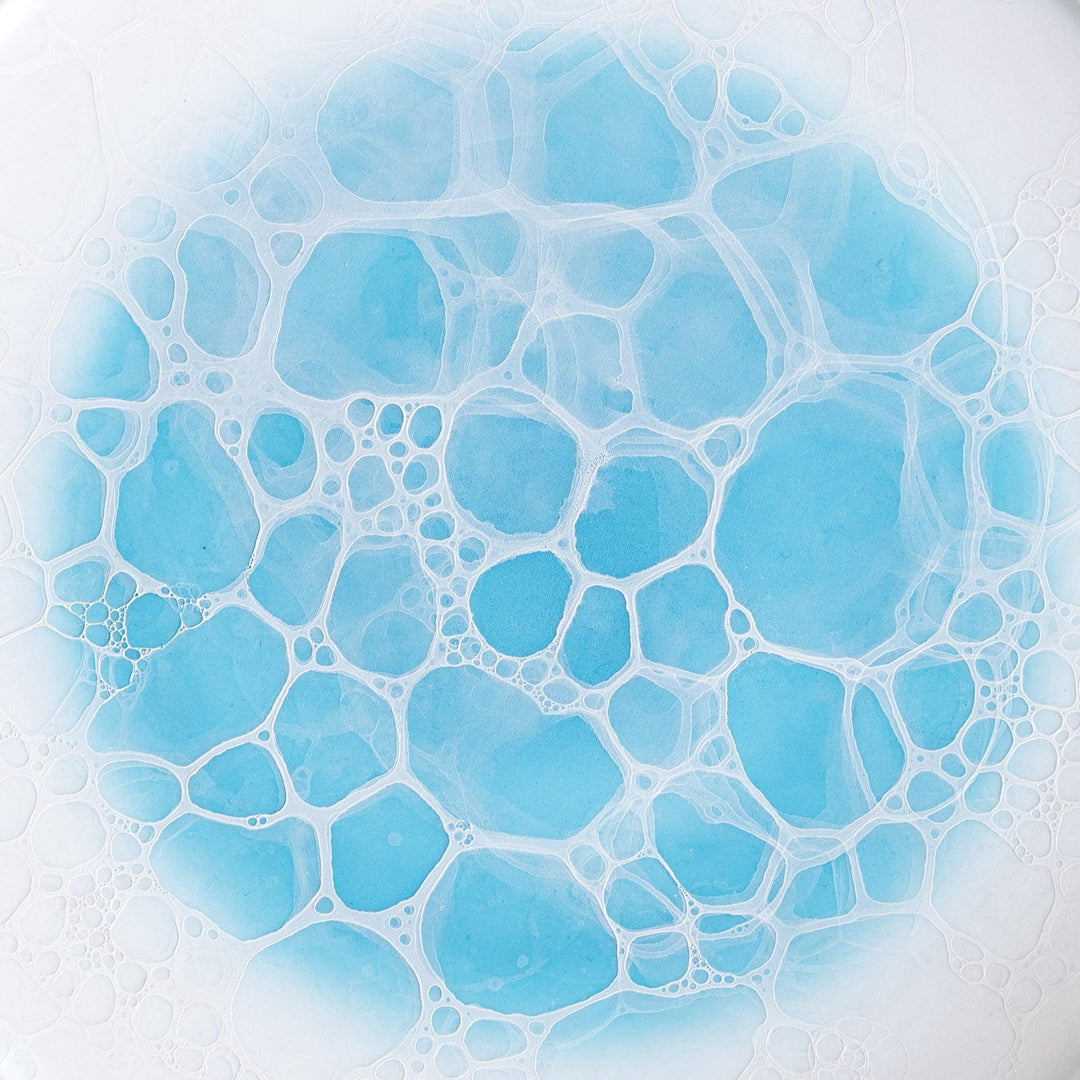 A white salad plate featuring a unique bubble design in shades of blue, resembling frothy ocean waves.