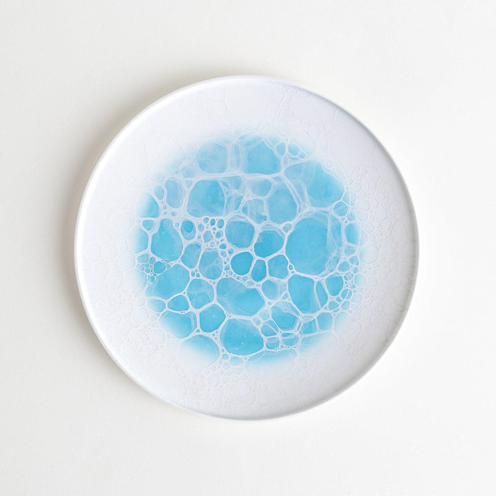 A white salad plate featuring a unique bubble design in shades of blue, resembling frothy ocean waves.