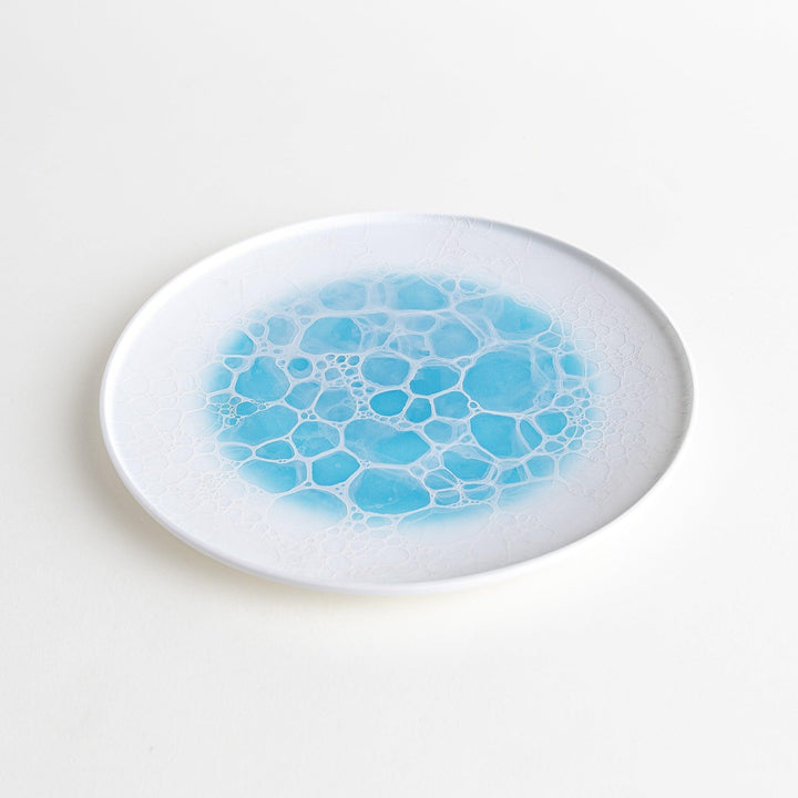 A white salad plate featuring a unique bubble design in shades of blue, resembling frothy ocean waves.